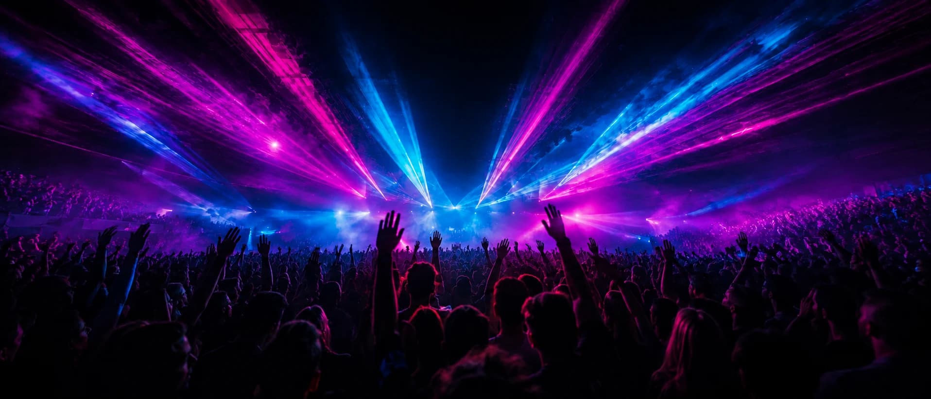 A concert crowd with waves of magenta and cyan light rippling through the air around them